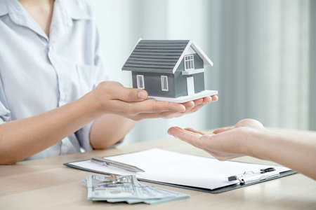 Hand a real estate agent, hold the home model, and explain the business contract, rent, buy, mortgage, loan, or home insurance to the buyer woman.の写真素材