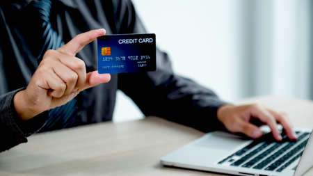 Businessman hand holding credit card to online shopping from home with laptop, payment e-commerce, internet banking, spending money for next holidays.の写真素材