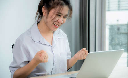 Young Asian woman chatting and talking with a friend on an online conference meeting with a video call on the laptop computer from home.の写真素材
