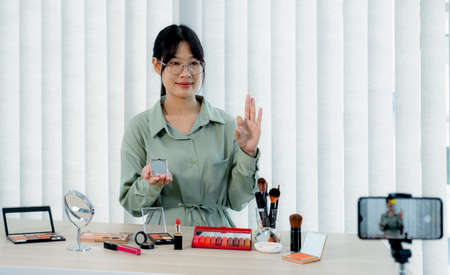 Beautiful Asia female vlogger is showing cosmetics makeup products while recording video and giving recommended for her beauty blog with digital smartphone.の写真素材