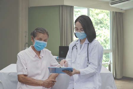 The doctor explained the health examination results to the elderly patient, They both wore masks due to the covid 19 epidemic.の写真素材