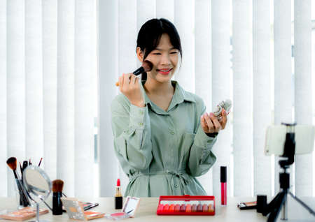 Beautiful Asia female vlogger is showing cosmetics makeup products while recording video and giving recommended for her beauty blog with digital smartphone.の写真素材