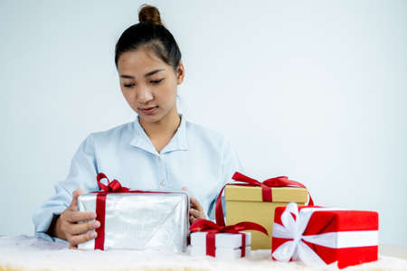 Woman in a blue shirt holding a white gift box tied with a red ribbon present for the festival of giving special holidays like Christmas, Valentine's Day.の写真素材