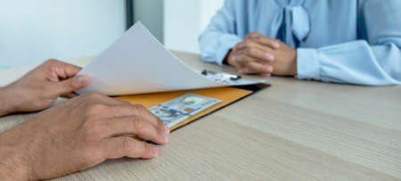 The hands of businessmen who bribe government officials to sign contracts for business projects put money under contract files, ideas of corruption and anti-bribery.の写真素材