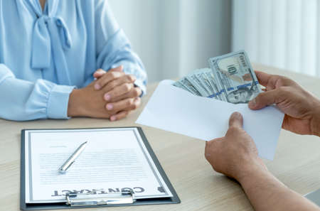 The hands of businessmen who bribe government officials to sign contracts for business projects hold...