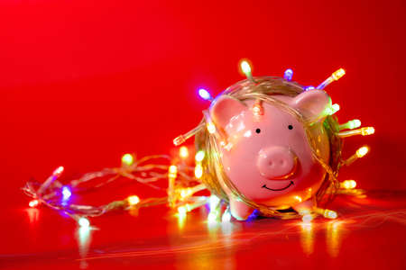 Pink piggy bank with Christmas string lights on happy December festival in Red background, Enjoy savings for spending money on the holiday's concept.の写真素材