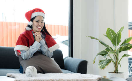 Beautiful Asian woman in Santa costume sitting on the sofa, concept Christmas and New Year.の写真素材