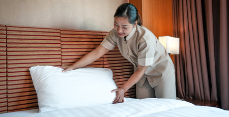 Hotel maid making the bed in the luxury hotel room ready for tourist travel.の写真素材