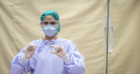 The doctor was wearing a mask, glasses and a hooded robe holding a vaccine bottle.の写真素材