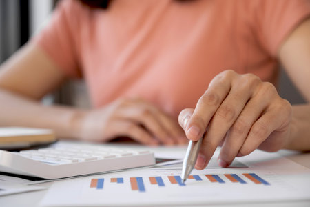 Asia woman hand holding pen, analysis the graph with calculartor and laptop at the home office for...
