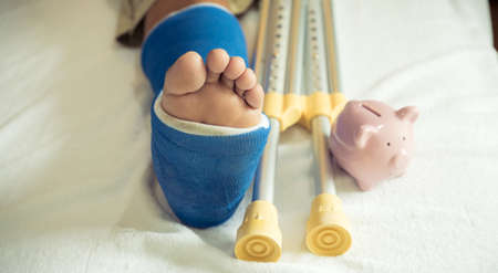 Man's leg uses crutches to walk after surgery recovery injury broken bones with pink piggy bank.