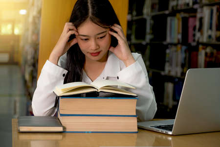 Young Asian female college students eyes reading book research and learn from textbooks in the...
