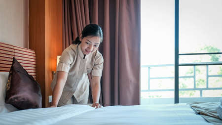 Hotel maid making the bed in the luxury hotel room ready for tourist travel.の写真素材