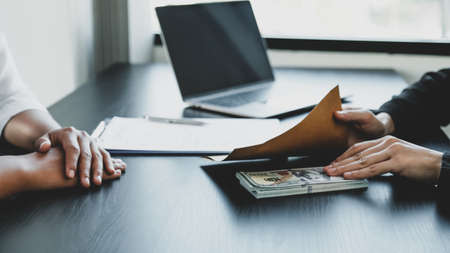 Businesswoman hand holding bribe money to government officials sign contracts for business projects, put money under envelope, ideas of corruption and anti-bribery.の写真素材