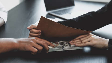 Businesswoman hand holding bribe money to government officials sign contracts for business projects, put money under envelope, ideas of corruption and anti-bribery.の写真素材