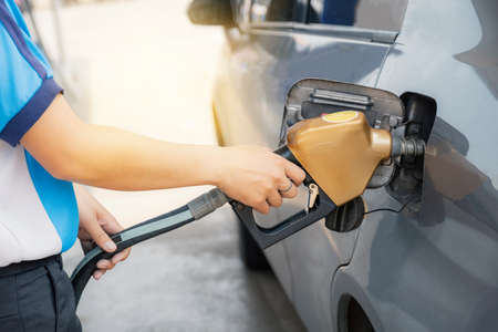 Worker hand holding golden nozzle pump gun petrol from oil pump in the car tank to refueling.の写真素材