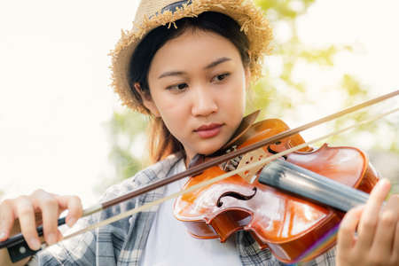 Close-up portrait of Young Asia woman music violinist play violin, relax in the garden with peace of mind.の写真素材