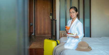 Picture of businesswoman eating fruits and drink orange juice on the bed in the luxury hotel room,...