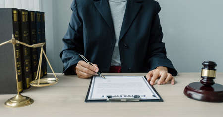 The woman lawyer is sitting at the desk in the office with a justice scale and gavel hammer. Study the law in business disputes to give advice to customers.の写真素材