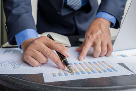 Businessman hand holding pen, analysis the graph with laptop at the home office for setting...