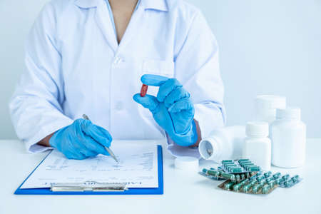 Doctor or nurse hand holding medicine pill and write a prescription at the pharmacy office,...