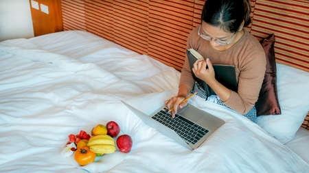 Picture of tourists used laptop and eating fruits on the bed in the luxury hotel room, healthy food concept.の写真素材