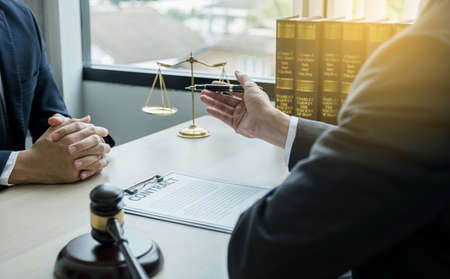 Lawyer hand holding pen and providing legal consult business dispute service to the man at the office with justice scale and gavel hammer.の写真素材