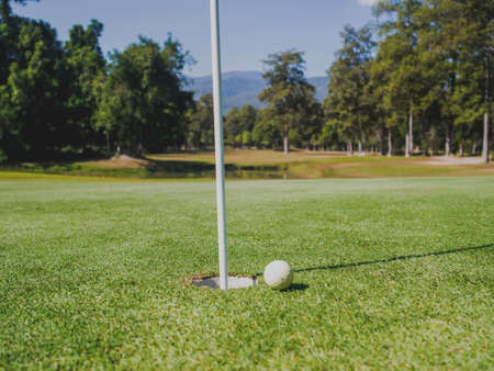 Photo of white golf ball on grass with hole and blue sky background.の写真素材