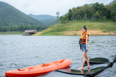 Asian girls in orange life jacket with the backdrop of water and mountains Ready for travel as a hobby in mae ngat dam, chiangmaiの写真素材