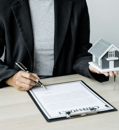 Hand a real estate agent sign with home model, key and explain the business contract, rent, buy,...