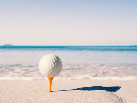 The golf ball is on the tee, embroidered on the sand beach with the sea in the background.の写真素材
