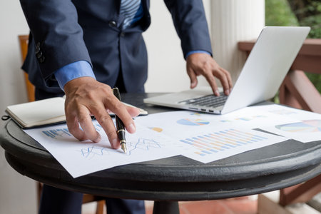 Businessman hand holding pen, analysis the graph with laptop at the home office for setting...