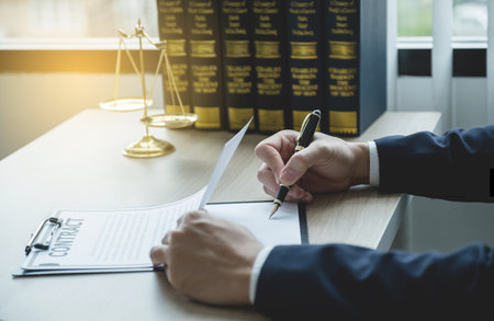 Lawyer hand holding pen and providing legal consult business dispute service at the office with justice scale and gavel hammer.の写真素材