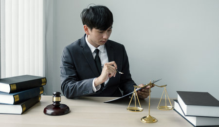 The man lawyer is sitting at the desk in the office with a justice scale and gavel hammer. Study the law in business disputes to give advice to customers.の写真素材