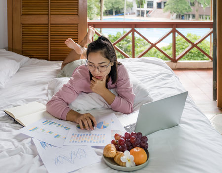 young woman used laptop video conferences and eating fruits on the bed, healthy food and work from home concept.の写真素材