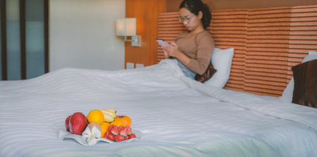 Fruits in tray in front of tourists used smartphone on the bed in the luxury hotel room.の写真素材