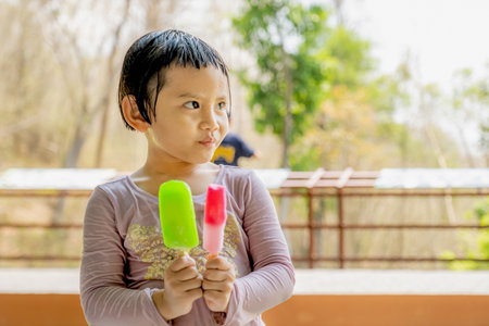 The happy kid girl in a wet shirt eating ice cream  in the natural outdoor background.の写真素材