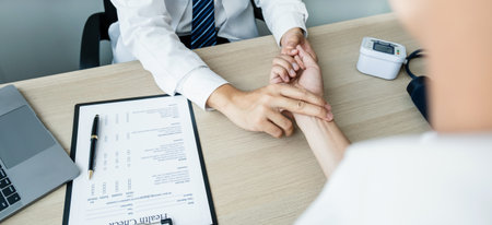 The doctor examines the patient's pulse by hand and records the results, health medical checkup concept.の写真素材