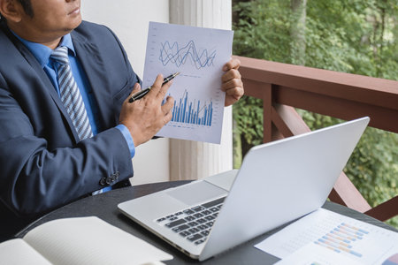 Businessman hand holding pen, analysis the graph with laptop at the home office for setting challenging business goals And planning to achieve the new target.の写真素材