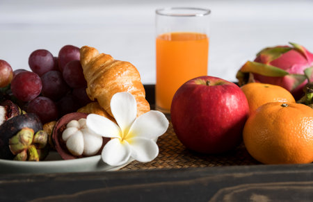 Breakfast, fruit, croissants, orange juice, in a black wooden tray, on a white bedsheet, Healthy food concept.の写真素材