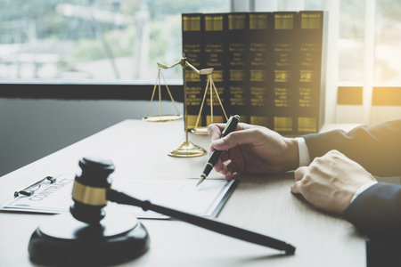 Lawyer hand holding pen and providing legal consult business dispute service at the office with justice scale and gavel hammer.の写真素材