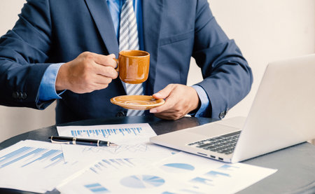 Businessman hand holding coffee cup, analysis the graph with laptop at the home office for setting challenging business goals And planning to achieve the new targetの写真素材