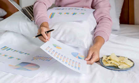 young woman hand holding pen used laptop video conferences and eating snack on the bed, healthy food and work from home concept.の写真素材