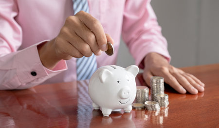Businessman hand putting coin into white piggy bank, step up start up business to success, Saving money for future plan and retirement fund conceptの写真素材