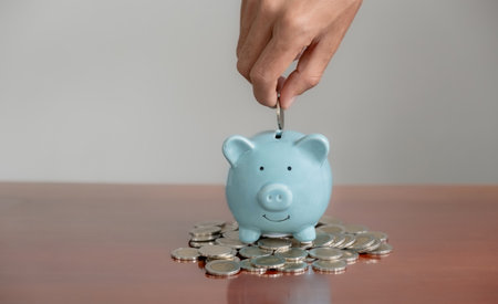 Businessman hand putting coin into blue piggy bank with coins pile, saving money for future investment plan and retirement fund concept.の写真素材