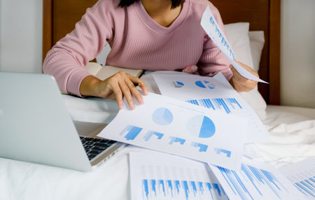 Business women bookkeeper hand holding pen and use laptop doing account for paying tax on on the bed, work from home concept.の写真素材