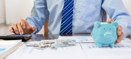 Businessman hand use calculator to check income and expenses to account with piggy bank and dollar notes, start-up businesses to success, Saving money for future plan and retirement fund concept.の写真素材