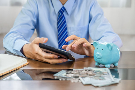 Businessman hand use calculator to check income and expenses to account with piggy bank and dollar notes, start-up businesses to success, Saving money for future plan and retirement fund concept.の写真素材