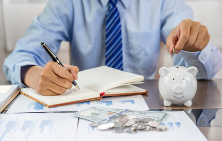 Businessman hand putting coin into blue piggy bank, saving money for future investment plan and retirement fund concept.の写真素材