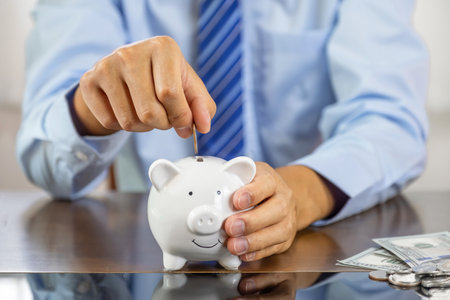 Businessman hand putting coin into blue piggy bank, saving money for future investment plan and retirement fund concept.の写真素材